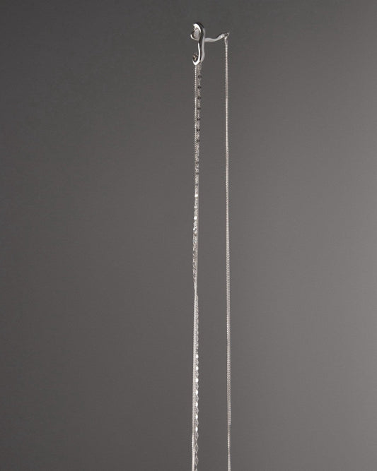 Close-up of a sculptural sterling silver ear cuff with textured hanging chains, minimalist modern jewelry design