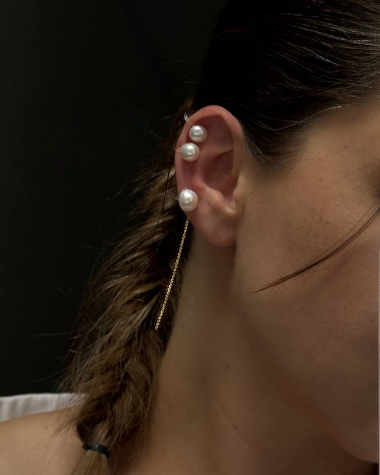 Model wearing a pearl ear cuff set with round pearls and a baroque pearl cuff with a dangling gold chain