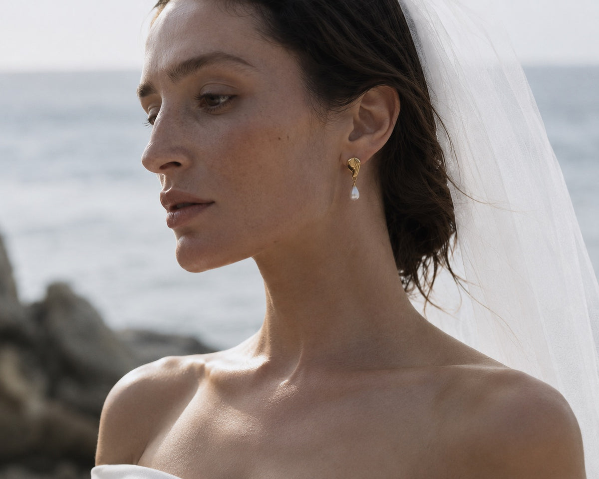 Close-up of a bride wearing DEW gold-plated sculptural earrings with dangling natural pearls