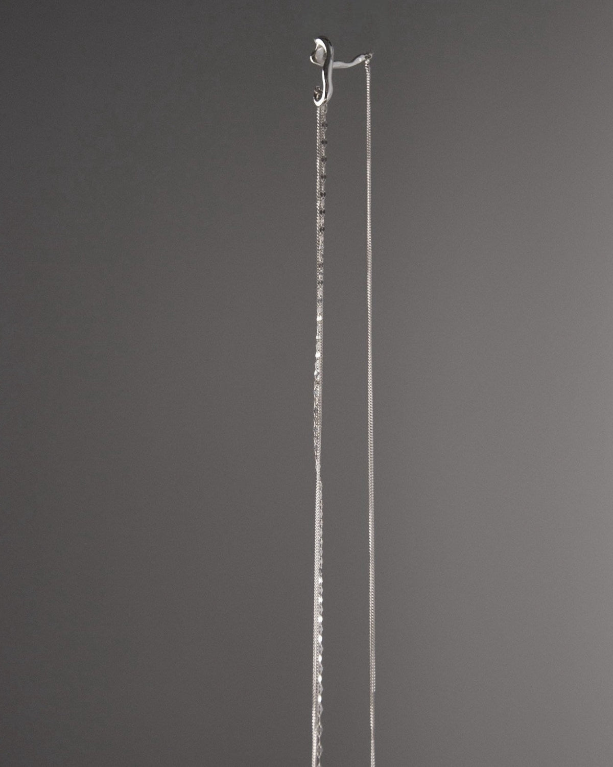 Close-up of a sculptural sterling silver ear cuff with textured hanging chains, minimalist modern jewelry design