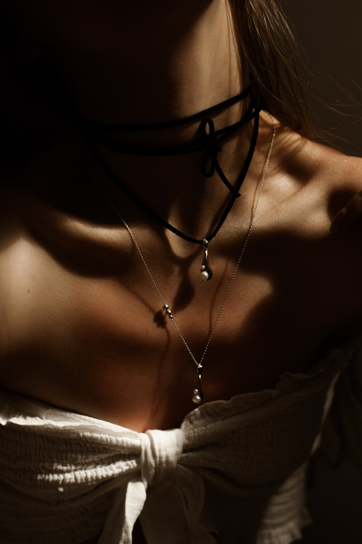 Sculptural Tear Drop pendant in polished sterling silver with natural pearls, styled on a black velvet cord against a woman’s décolletage
