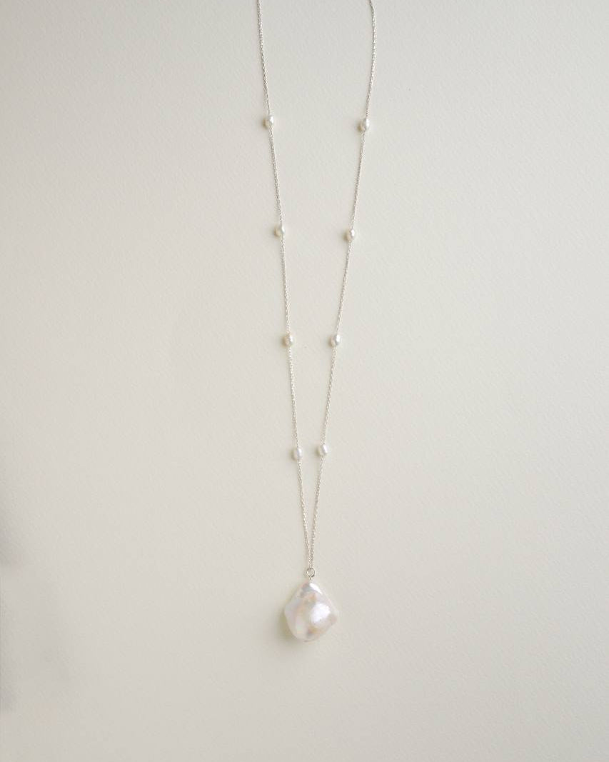 Long sterling silver necklace with a large baroque pearl pendant and small pearls spaced along the chain