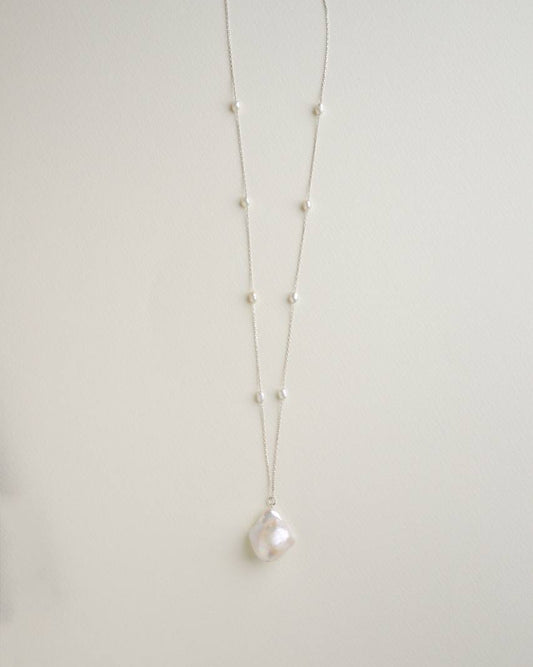 Long sterling silver necklace with a large baroque pearl pendant and small pearls spaced along the chain
