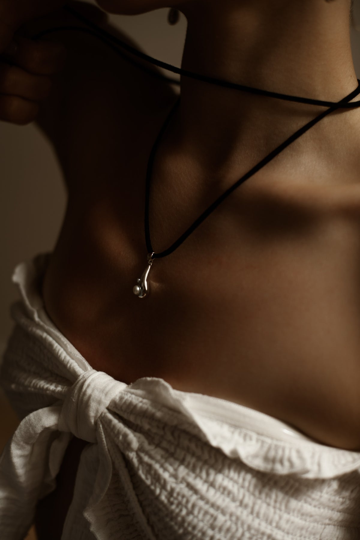 Tear Drop rhodium-plated sterling silver pendant with natural pearls on a black velvet cord, worn around a woman’s neck