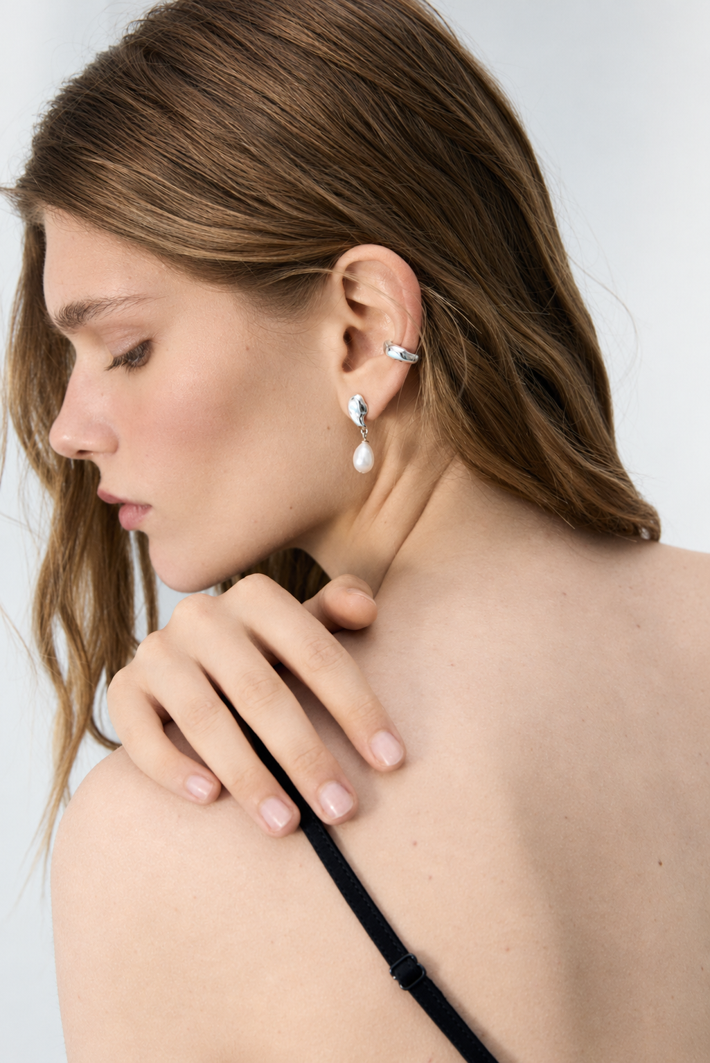 Model wearing DEW sterling silver pearl drop earrings with fluid sculptural studs and dangling natural pearls