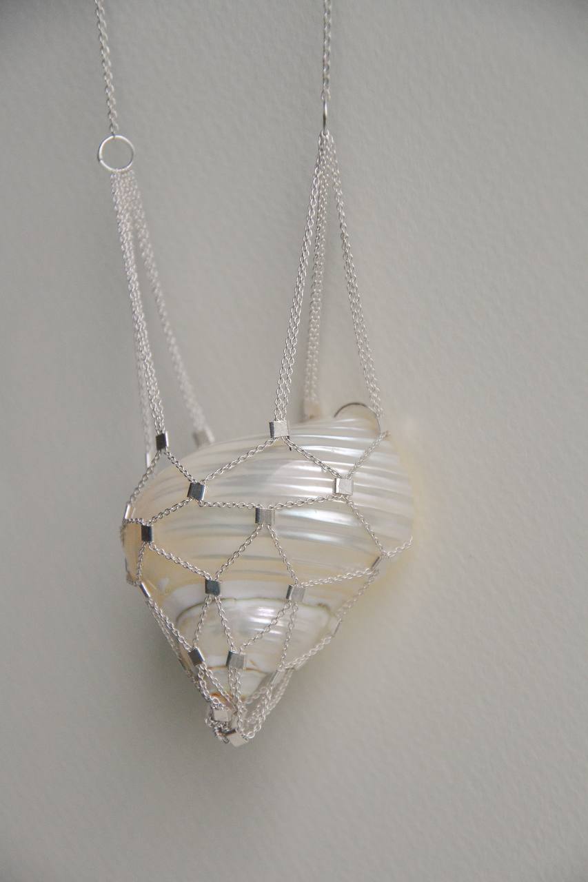 Close-up of the woven silver chain net surrounding the shell pendant
